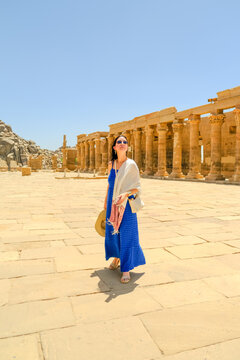 Woman in a blue dress with a white scarf holding a hat at the Philae Temple in Egypt