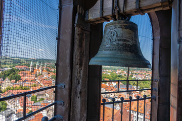 A large, detailed bell in a tower overlooking a picturesque cityscape