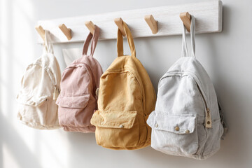 Neutral-toned fabric backpacks hanging neatly on wooden wall hooks in minimalist setting, symbolizing order and back to school. Copy space