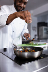 African american expert in a kitchen prepares a dish with fresh basil and parsley, showcasing...