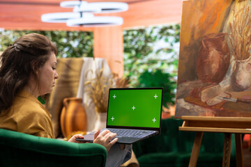 Female artist using green screen sitting in her art and craft atelier, looking at her fresh new...