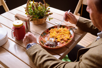 Unrecognizable man eating scrambled eggs with ham and beans with cheese and beet juice
