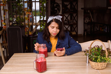 hispanic woman watching her cell phone in a restaurant while drinking juice