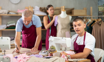 Working day in sewing workshop, textile industry. Guy master sew clothes in sewing machine, senior...