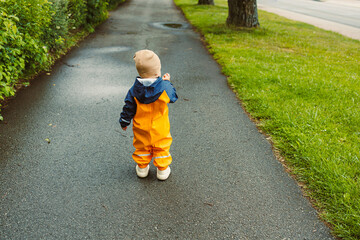 An adorable child dressed in a bright raincoat is joyfully walking along a charming pathway that is...