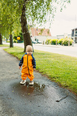 A cheerful toddler dressed in vibrant rain gear is joyfully splashing in a puddle during an...