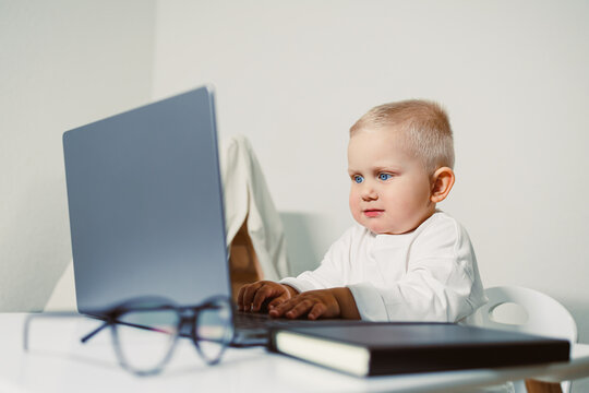 A Curious Baby is Tapping on a Laptop Keyboard while playing in a Modern Workspace, showcasing their innate curiosity and creativity in a digital world that promotes learning and discovery