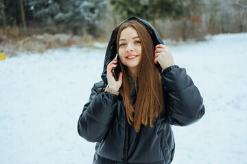 On a serene winter day, a young woman enjoys the snowy landscape while chatting on her phone,...