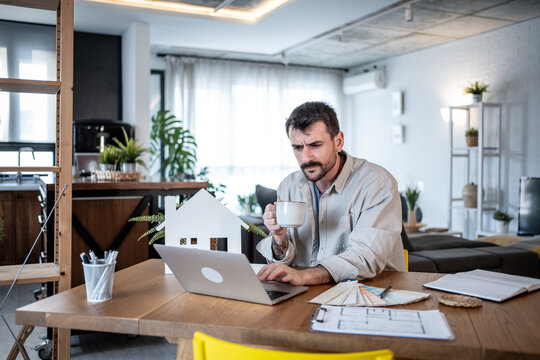 Architect drinking coffee and working on laptop at home office - Powered by Adobe
