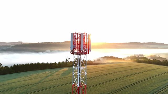 Aerial drone footage of a telecommunication tower enveloped in morning fog at sunrise. Soft golden light, misty atmosphere, calm nature, technology blending with environment, peaceful and inspiring ur