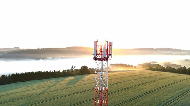 Aerial drone footage of a telecommunication tower enveloped in morning fog at sunrise. Soft golden light, misty atmosphere, calm nature, technology blending with environment, peaceful and inspiring ur