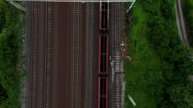 Aerial drone footage of a moving freight train traveling through diverse landscapes. The powerful locomotive pulls cargo cars along winding tracks, showcasing industrial transport and logistics effici