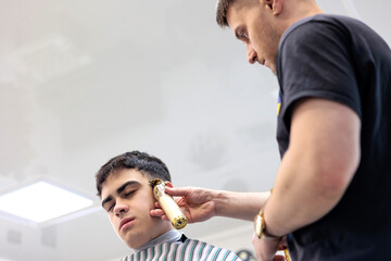 Professional Barber Giving a Haircut to a Young Client with an Electric Trimmer. Young Male Barber...