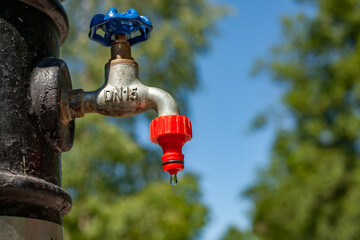 Outdoor metal water tap with a red fitting and a single droplet hanging, symbolizing water waste or...