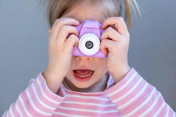 Preschool girl plays with toy camera, pink striped shirt, learning photography, early creativity,...