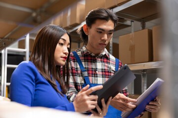 Asian employees organizing taped boxes and goods in a storage room, working on a retail small...