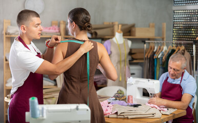 Guy seamstress employee works with girl client, takes measurements of clients body parts, collects...