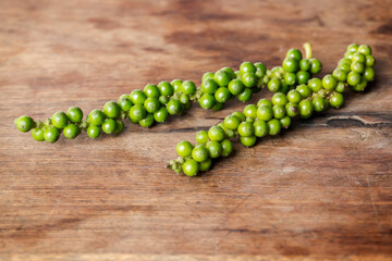 Unprocessed fresh green peppercorns on wooden table