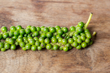 Unprocessed fresh green peppercorns on wooden table