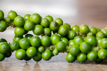 Unprocessed fresh green peppercorns on wooden table