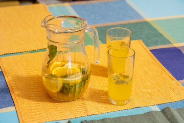 Glass jug pitcher of homemade cold lemonade with lemon slices mint leaves colorful vibrant yellow...