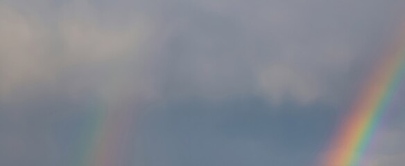 Two vibrant rainbows arching across a cloudy sky, following a refreshing rain shower, create a...