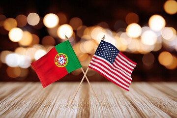 Obraz premium miniature Portugal and USA flags crossed on polished wooden surface with warm bokeh background