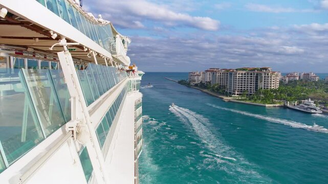 Cruise ship departing Port of Miami, passing luxury waterfront condos and calm turquoise waters under a vibrant sky. Dynamic aerial view captures the start of a tropical journey.
