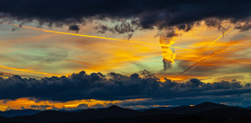 Dramatic Sunset Sky with Contrails and Vertical Cloud Light Column Over Mountain