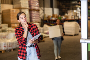 Caucasian girl checking quantity of goods in storehouse, making inventory.