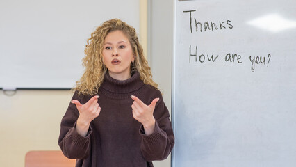 Caucasian female teacher communicates in Russian sign language with students. 