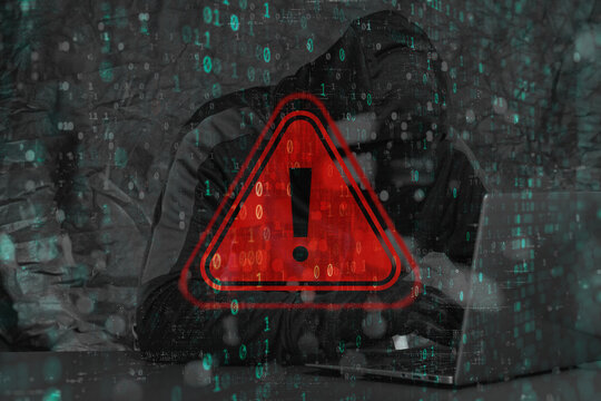 A hooded hacker behind a laptop with a red glowing warning with a triangle and exclamation mark. Binary code overlays the scene, emphasizing the concept of data leakage and cybercrime.
