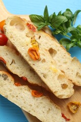 Pieces of delicious focaccia with tomatoes and basil on light blue table, flat lay