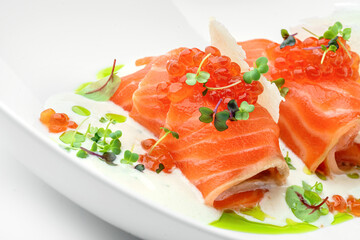 Salmon rolls and red caviar with sauce and greens on plate isolated on white background. Fish and seafood, close up, top view