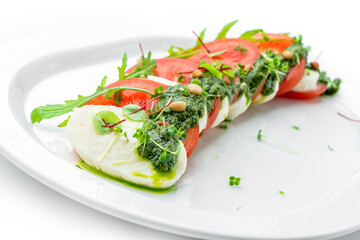 Fresh italian Caprese salad with tomatoes, mozzarella cheese and basil in plate isolated on white background, top view, close up