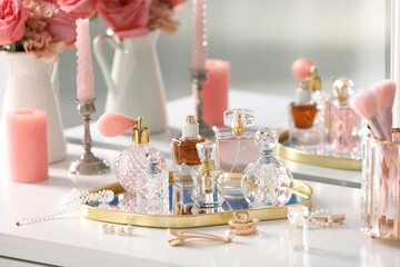 Bottles of different perfumes, accessories and flowers on dressing table indoors