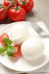 Tasty mozzarella cheese balls, tomatoes and basil on wooden table, closeup