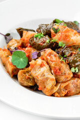 Dolma, cabbage rolls, grape leaves with filling with sour cream in plate isolated on white background. Traditional dishes, top view, close up