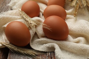 Raw eggs, fabric and spikes of wheat on wooden table, closeup