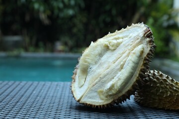 Fresh ripe durian on wicker table near swimming pool outdoors, closeup. Space for text