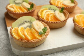 Tartlets with fruits and mint on gray textured table, closeup. Delicious dessert