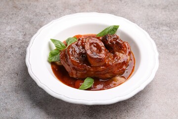 Traditional ossobuco dish with beef steak, sauce and basil on grey table, closeup