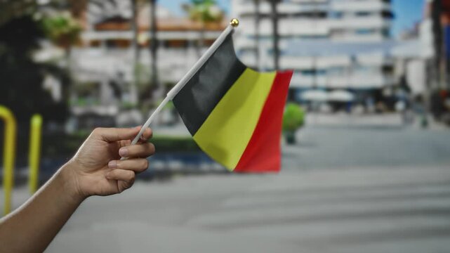 Hand holds belgian flag in outdoor city street setting, signifying national pride and cultural identity.