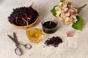 Cup of hot tea, branches of elderberry and jam from it close-up