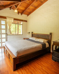 Bright rustic bedroom with wooden bed frame, ceiling beams, and natural light in Ecuador lodge....