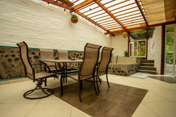 Indoor patio with dining table and chairs, stone hot tub, white walls, wood beam roof, and natural...