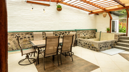 Covered patio area with metal dining table and chairs, stone hot tub, white walls, and wood beam roof in Ecuador.