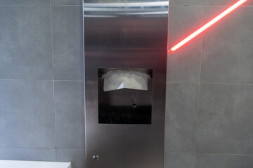 A metallic sanitary disposal unit is mounted on a wall with a red laser indicator, highlighting its...
