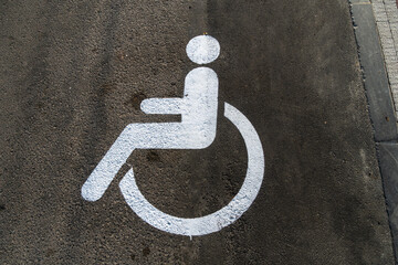 A white accessibility symbol is painted on a gray concrete surface, designating a parking space for...