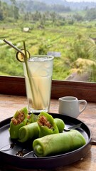 Vertical image of a close up of green Indonesian coconut pancakes and homemade iced ginger tea served inside a restaurant in Sidemen with natural light at daytime on Bali in Indonesia, Asia.